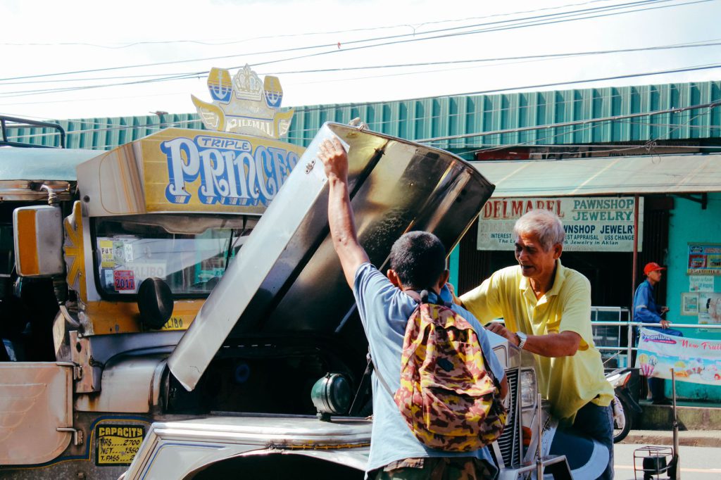 People interacting with a jeepney on a sunny street in Altavas, Philippines.