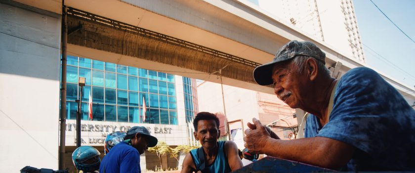 Men engaged in a street conversation near the University of the East building.
