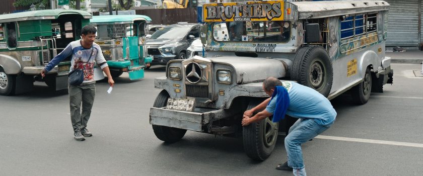 A jeepney being repaired on a busy Manila street, showcasing urban life in the Philippines.
