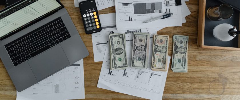 Overhead view of financial documents, cash, and technology on a wooden desk.
