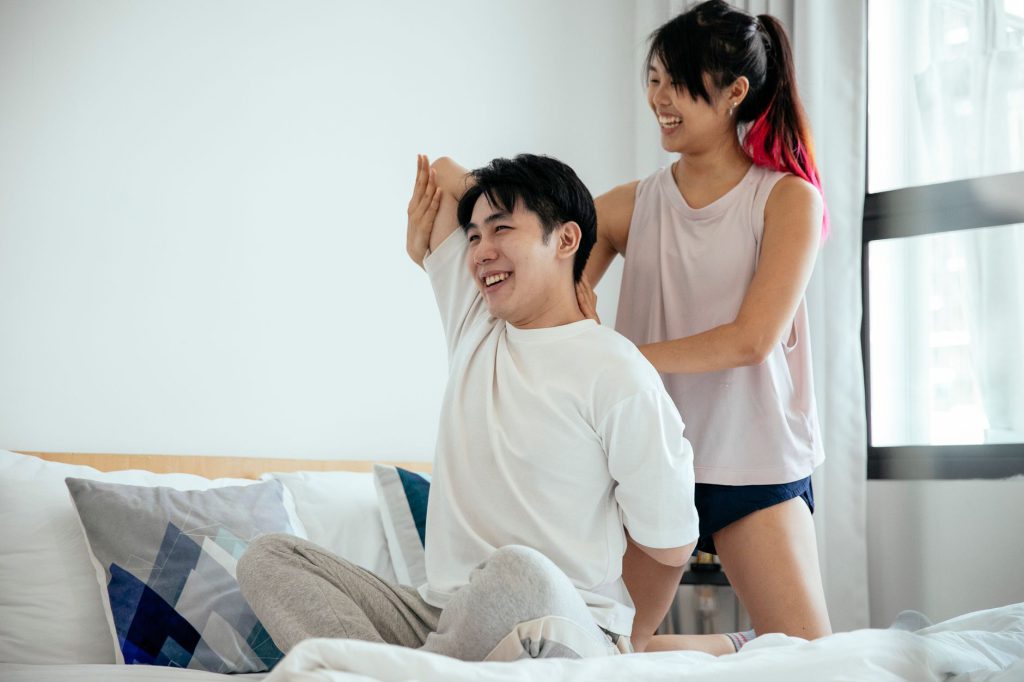 Happy Asian couple practicing Cow face pose while doing Gomukhasana yoga pose in bed at sunlight in morning
