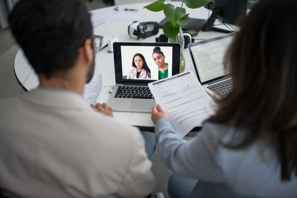 Two professionals conduct a virtual job interview using laptops in a modern office.