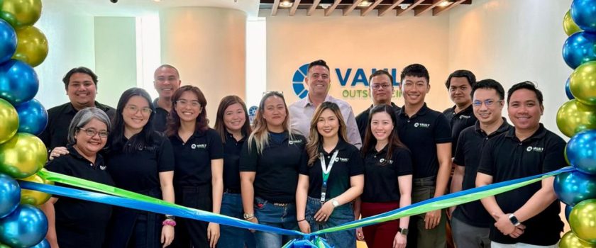Vault Outsourcing staff in black company shirts standing behind a blue and green ribbon at an office opening