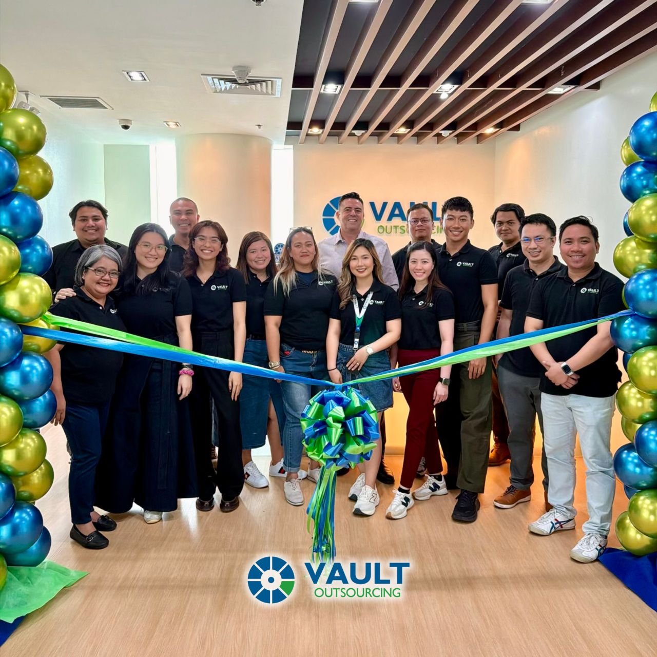 Vault Outsourcing staff in black company shirts standing behind a blue and green ribbon at an office opening