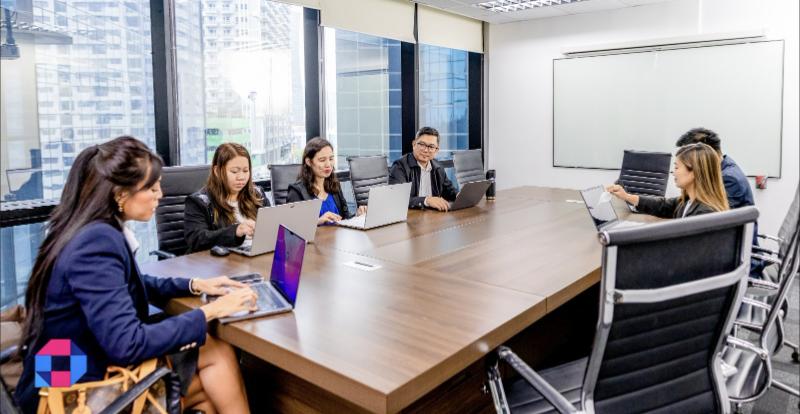 Six CPS Asia Pacific team members working on laptops around a long boardroom table in an office with city views