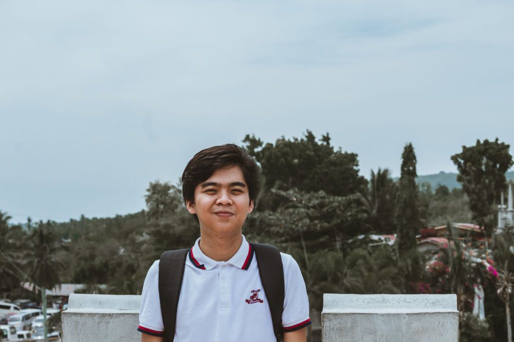 Young Asian man smiling outdoors in Cebu City with trees in the background.