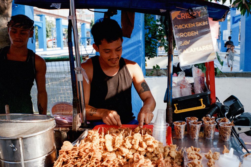 A street vendor serves skewers and crispy snacks at a vibrant food stall in Manila, Philippines.