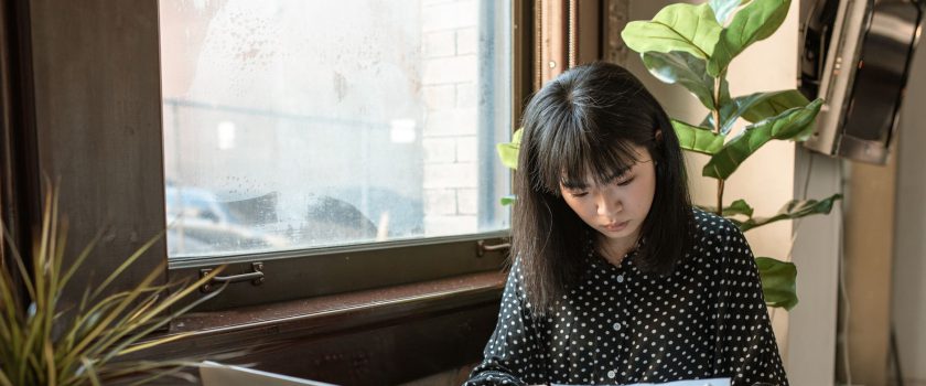 Asian businesswoman reviewing documents in a modern office setting with natural light.