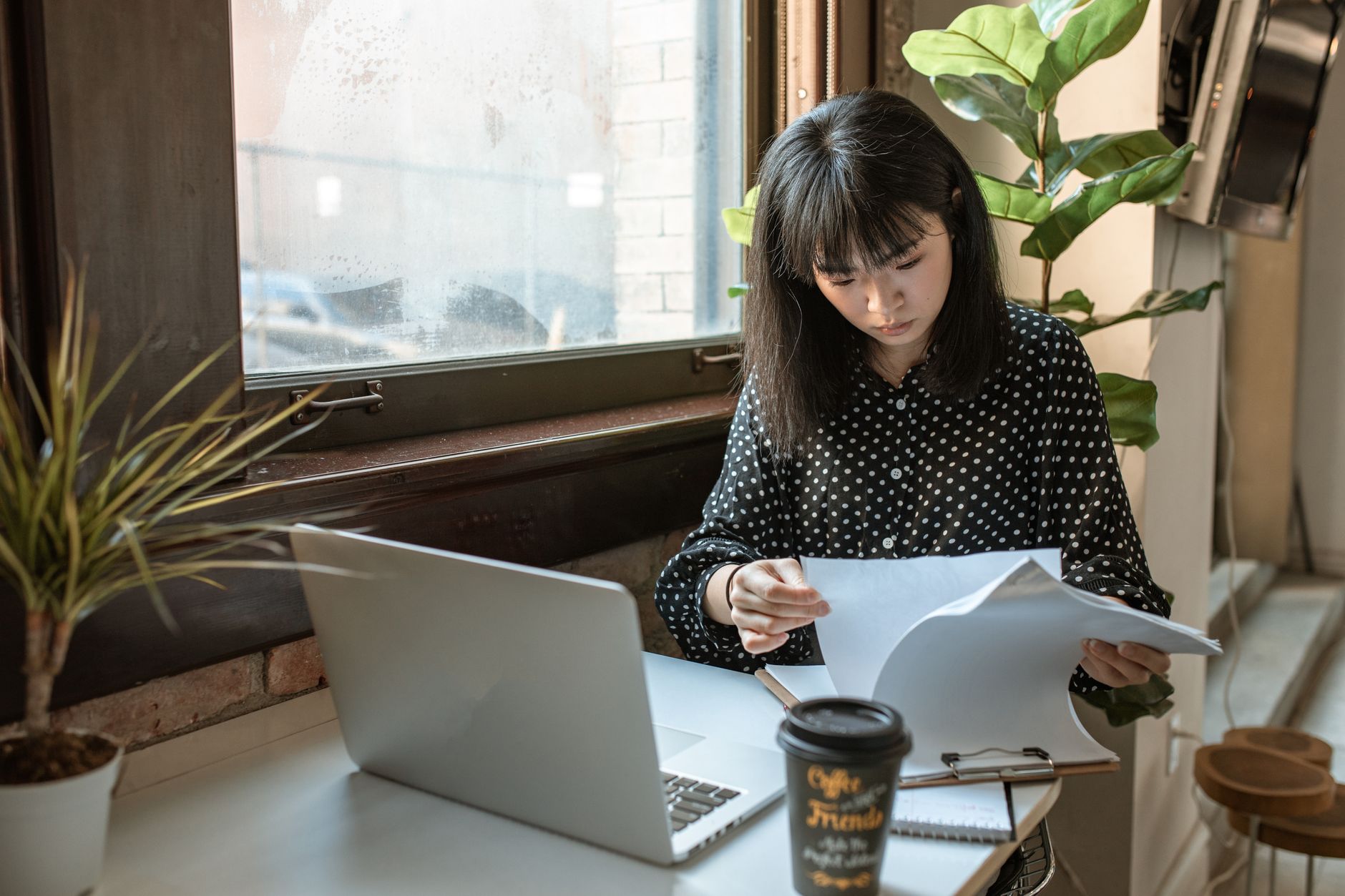 Asian businesswoman reviewing documents in a modern office setting with natural light.