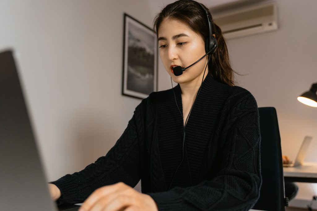 A woman working in a call center, using a laptop and headset for customer service assistance.